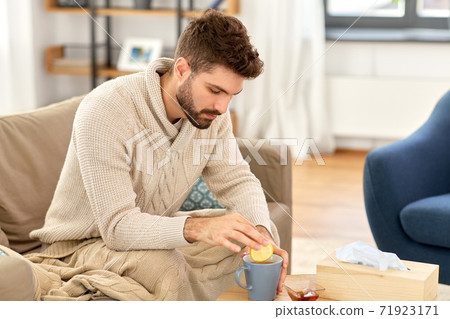 sick young man in blanket drinking hot tea at home 71923171