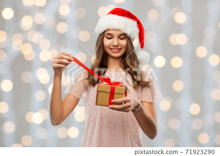 teenage girl in santa hat opening christmas gift teenage girl in santa hat opening christmas gift 71923290
