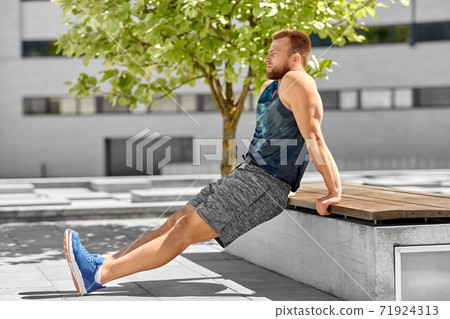 young man doing triceps dip on city street 71924313
