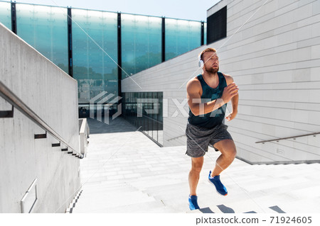 young man in headphones running upstairs outdoors 71924605