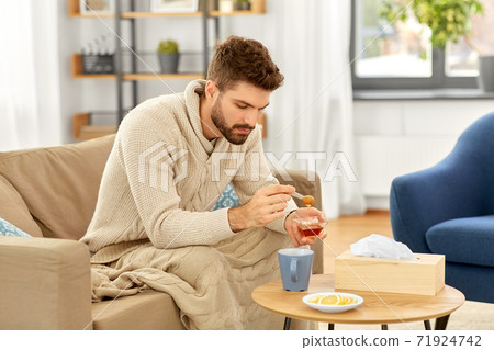 sick young man in blanket drinking hot tea at home sick young man in blanket drinking hot tea at home 71924742