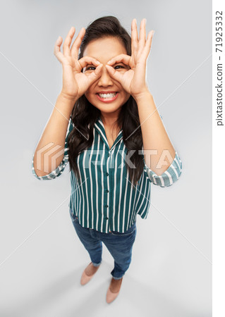smiling asian woman looking through finger glasses smiling asian woman looking through finger glasses 71925332