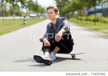 teenage boy sitting on skateboard on city street 71925492