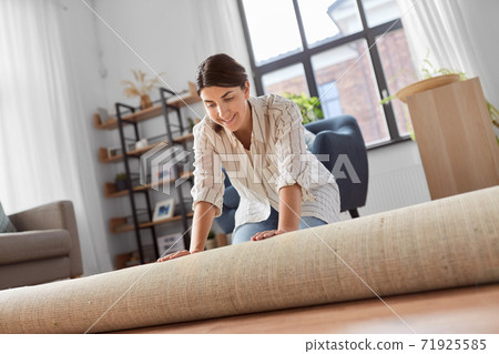 young woman unfolding carpet at home 71925585