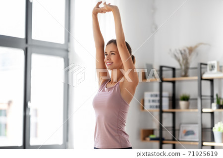 smiling young woman stretching arms at home 71925619