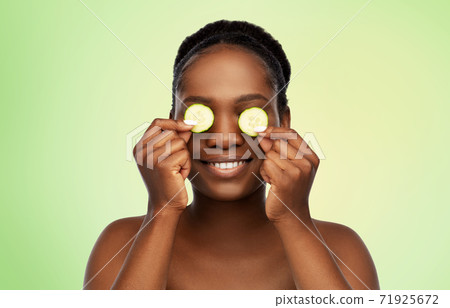 happy african woman making eye mask of cucumbers happy african woman making eye mask of cucumbers 71925672