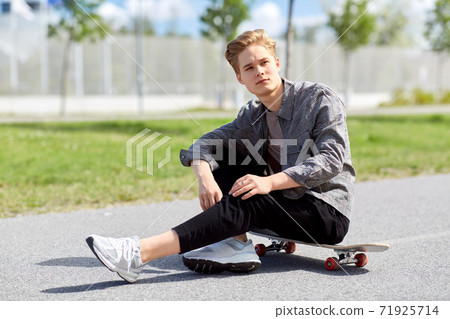 teenage boy sitting on skateboard on city street 71925714