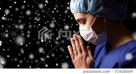 female doctor or nurse in face mask praying 71926084