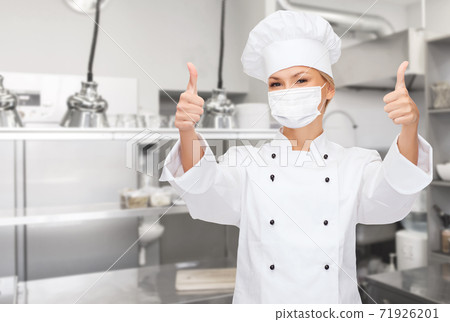 female chef in mask showing thumbs up at kitchen 71926201