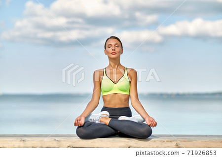 young woman meditating in lotus pose at seaside 71926853