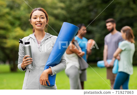 smiling woman with yoga mat and bottle at park smiling woman with yoga mat and bottle at park 71927863