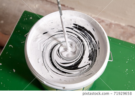 Worker is mixing paints in basket using mixer to paint walls. Worker is mixing paints in basket using mixer to paint walls. 71929658