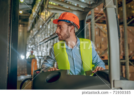 Young bearded worker in yellow vest looking concentrated 71930385