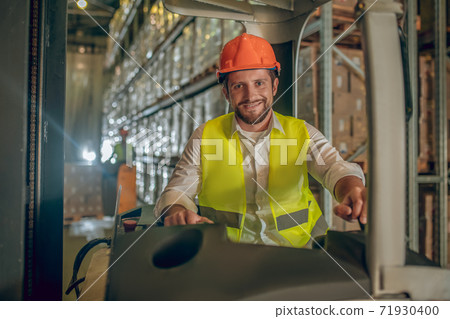 Young bearded worker sitting at the loader and smiling 71930400