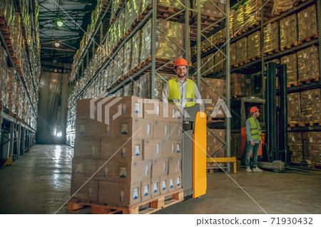 Two workers in helmets and vests working in the warehouse 71930432