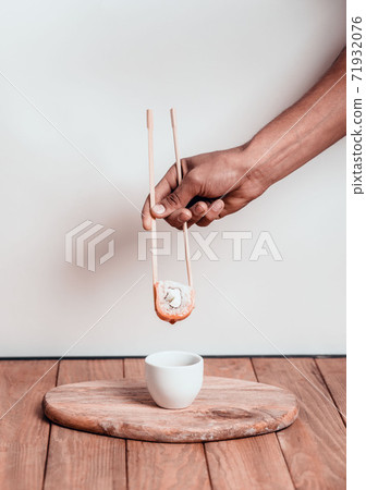 Hand holds sushi with chopstick over a bowl of soy sauce on a white background. Sushi menu. 71932076