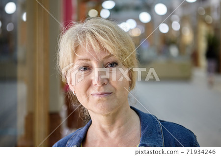 Serious beautiful old lady with blond hair in trade gallery. Serious beautiful old lady with blond hair in trade gallery. 71934246