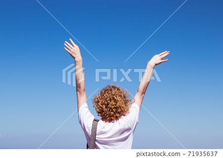 Woman raised her hands to the blue sky with copy space. Girl feeling happy to travel, joy of freedom concept 71935637