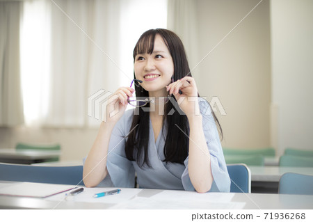 Beautiful female college student / young female employee sitting in a bright lecture room with glasses Beautiful female college student / young female employee sitting in a bright lecture room with glasses 71936268