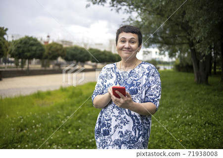 Happy middle-aged woman smiling speaks by phone on park natural background. 71938008