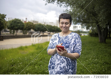 Happy middle-aged woman smiling speaks by phone on park natural background. 71938010