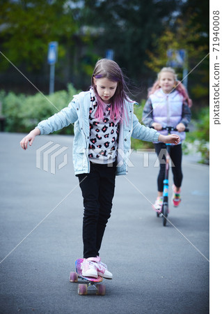Two pretty little sisters having fun together learning to skateboard outdoors. The concept of a healthy lifestyle. Kids sport 71940008
