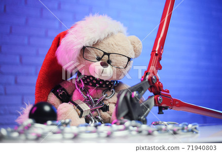 a toy bear wearing leather belts and a Santa Claus hat in the New year Christmas is chained and handcuffed an accessory for BDSM games next to a bolt cutter a toy bear wearing leather belts and a Santa Claus hat in the New year Christmas is chained and handcuffed an accessory for BDSM games next to a bolt cutter 71940803