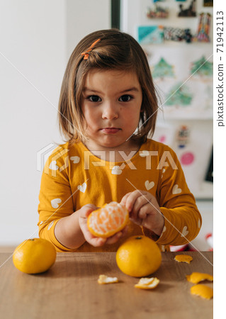 Caucasian girl peeling tangerines on kitchen counter. Healthy child diet. Immune boosting with 71942113
