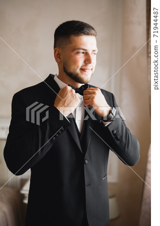 Grooms morning preparation. Handsome man getting dressed and preparing for the wedding Grooms morning preparation. Handsome man getting dressed and preparing for the wedding 71944487