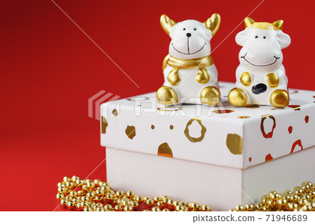 New year's toy of a bull and a cow with a gift on a red background. New year's toy of a bull and a cow with a gift on a red background. 71946689