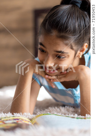 childhood, emotions, solitude, beauty concept - portrait of happy young minor cheerful joyful dark-skinned girl of middle eastern persian appearance 6-9 years old smiling cutely lying on bed indoors. 71950453
