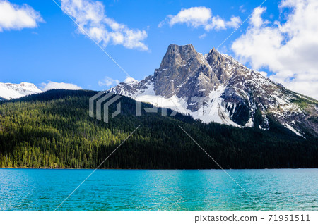 Mountain rising from dark forest under blue sky and clouds. Mountain rising from dark forest under blue sky and clouds. 71951511