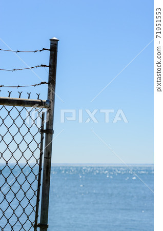 Edge of fence and barb wire against sky and water. 71951553
