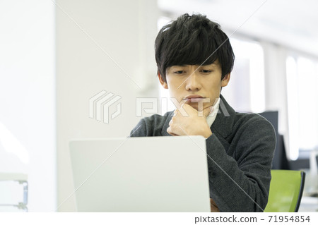 A man frowning while looking at a computer screen A man frowning while looking at a computer screen 71954854