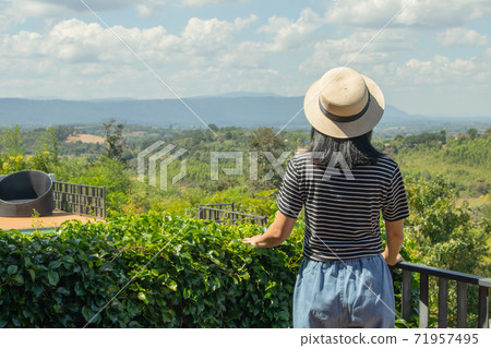 Asian woman wear weave hat and stand on wooden terrace. She feeling relax and happiness. Asian woman wear weave hat and stand on wooden terrace. She feeling relax and happiness. 71957495
