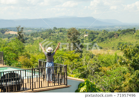 Asian woman wear weave hat and stand on wooden terrace. She feeling relax and happiness. Asian woman wear weave hat and stand on wooden terrace. She feeling relax and happiness. 71957496