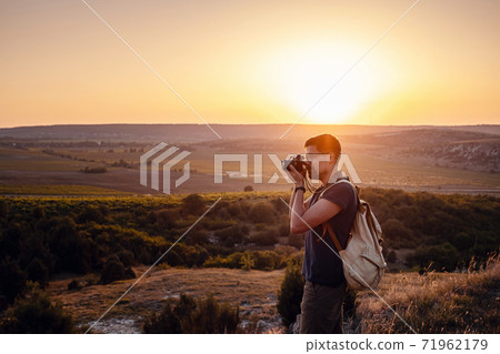 Man photographer with backpack and camera taking photo of sunset mountains Man photographer with backpack and camera taking photo of sunset mountains 71962179