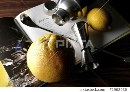 Make a cocktail with a shaker while looking at a cocktail book using grapefruit and lemon Make a cocktail with a shaker while looking at a cocktail book using grapefruit and lemon 71962986
