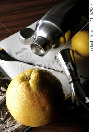 Make a cocktail with a shaker while looking at a cocktail book using grapefruit and lemon Make a cocktail with a shaker while looking at a cocktail book using grapefruit and lemon 71962989