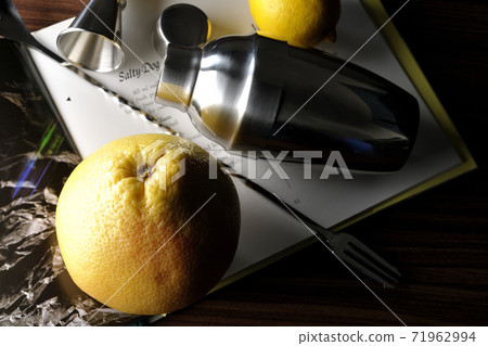 Make a cocktail with a shaker while looking at a cocktail book using grapefruit and lemon Make a cocktail with a shaker while looking at a cocktail book using grapefruit and lemon 71962994