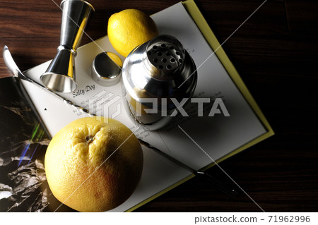 Make a cocktail with a shaker while looking at a cocktail book using grapefruit and lemon 71962996