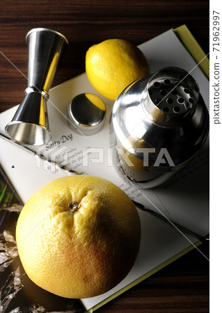 Make a cocktail with a shaker while looking at a cocktail book using grapefruit and lemon 71962997