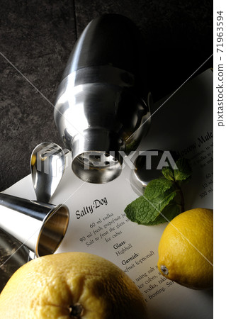Make a cocktail with a shaker while looking at a cocktail book using grapefruit, lemon and mint 71963594