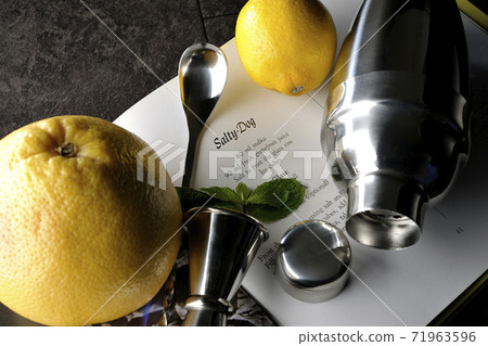 Make a cocktail with a shaker while looking at a cocktail book using grapefruit, lemon and mint 71963596