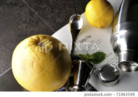 Make a cocktail with a shaker while looking at a cocktail book using grapefruit, lemon and mint Make a cocktail with a shaker while looking at a cocktail book using grapefruit, lemon and mint 71963599