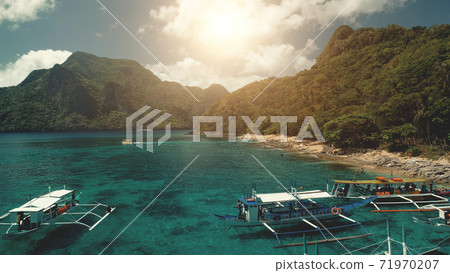 Sun green tropic forest mountain ranges at ocean bay. People rest on sand beach at passenger boats 71970207