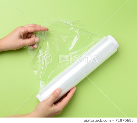 two female hands hold a roll of transparent cling film for packaging products 71970693