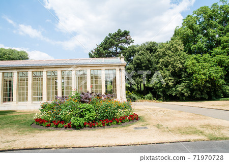 A historic stone, glass-enclosed building in Kew Gardens on the outskirts of London surrounded by greenery 71970728