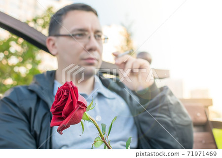 red rosebud in the hand of a thoughtful guy with glasses red rosebud in the hand of a thoughtful guy with glasses 71971469