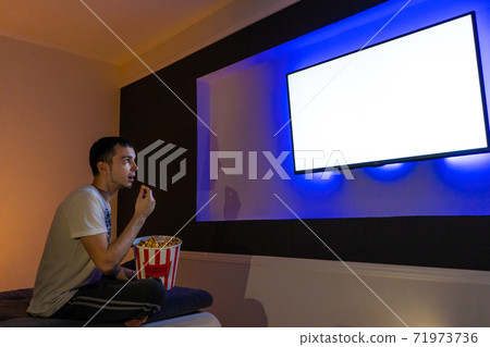 person watches a movie sitting on the couch with a bucket of popcorn person watches a movie sitting on the couch with a bucket of popcorn 71973736